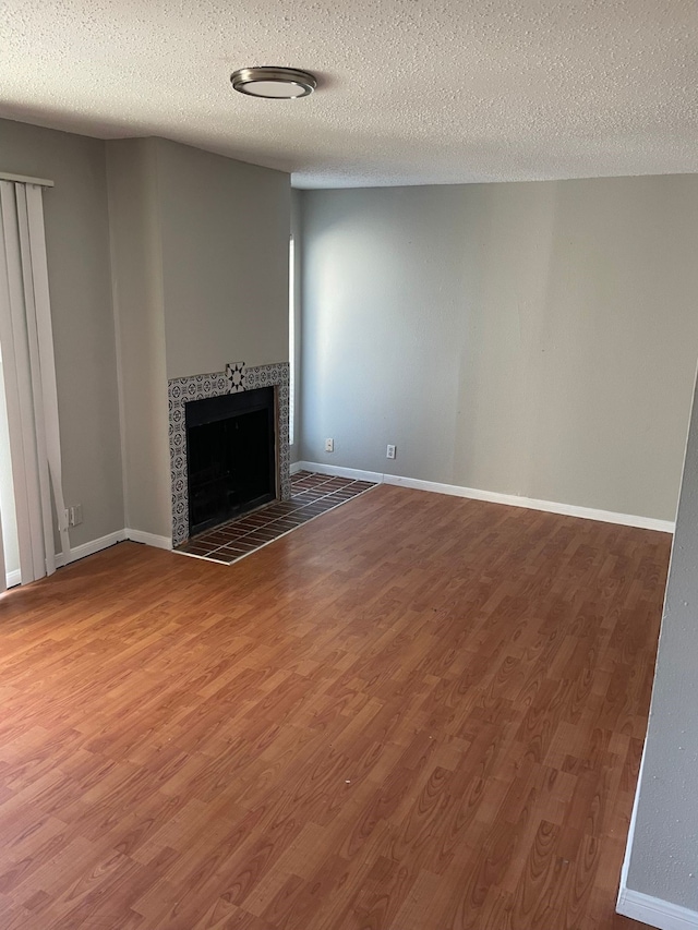 unfurnished living room with hardwood / wood-style floors, a textured ceiling, and a tiled fireplace