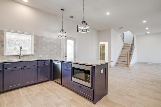 kitchen featuring light stone counters, a sink, appliances with stainless steel finishes, light wood-type flooring, and tasteful backsplash