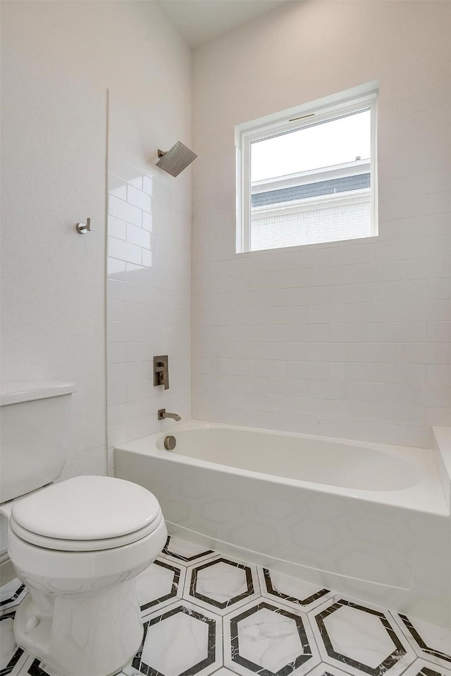 bathroom with tiled shower / bath combo, tile patterned floors, and toilet