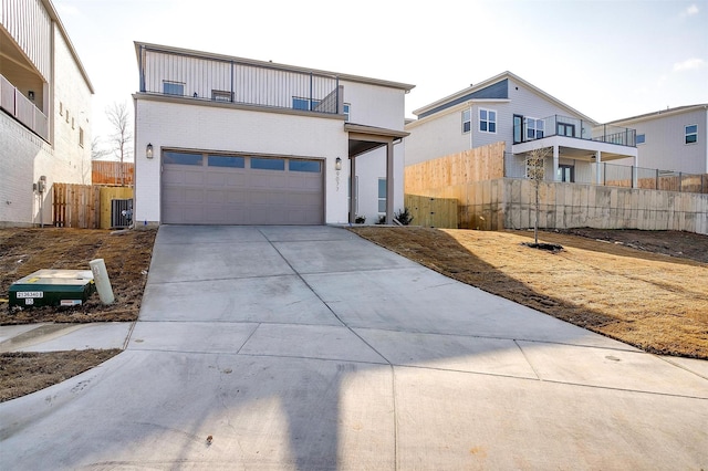 view of front of home with concrete driveway, a balcony, an attached garage, fence, and central air condition unit