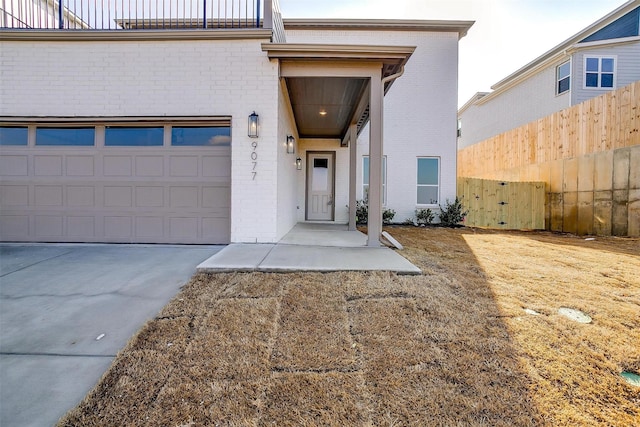 doorway to property featuring concrete driveway, brick siding, and fence