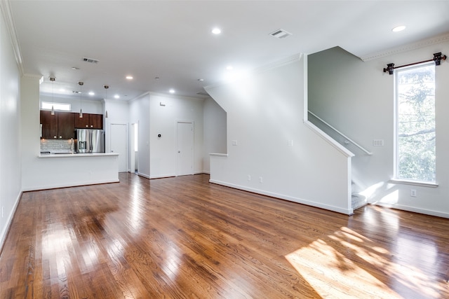 unfurnished living room with hardwood / wood-style flooring, a wealth of natural light, and ornamental molding