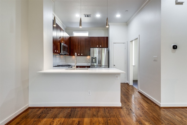 kitchen featuring crown molding, appliances with stainless steel finishes, dark brown cabinets, dark hardwood / wood-style flooring, and kitchen peninsula