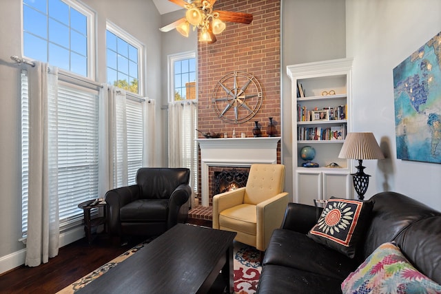 living room with ceiling fan, built in features, dark wood-type flooring, and a brick fireplace