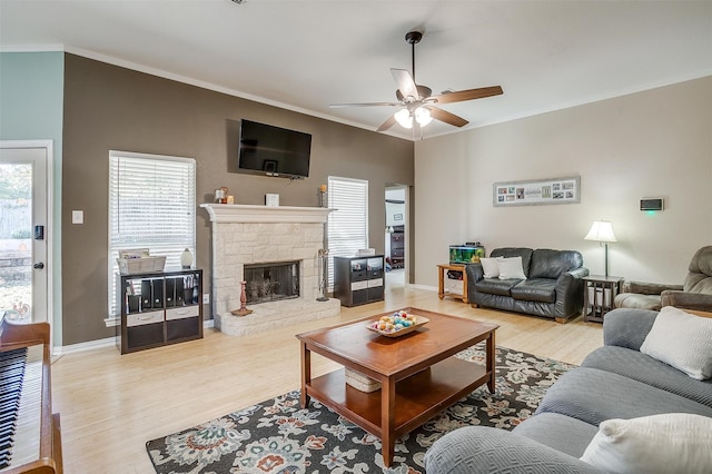 living room featuring ceiling fan, light hardwood / wood-style floors, a stone fireplace, and ornamental molding