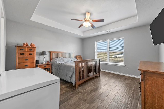 bedroom with dark hardwood / wood-style floors, a raised ceiling, and ceiling fan