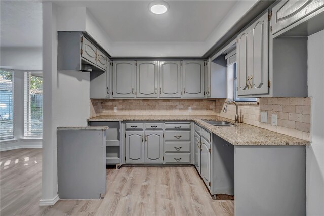 kitchen with gray cabinets, decorative backsplash, sink, and light wood-type flooring