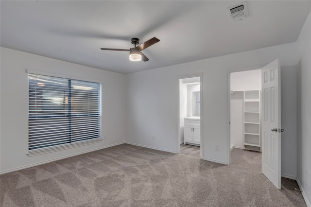 unfurnished bedroom with ensuite bath, a spacious closet, ceiling fan, light colored carpet, and a closet