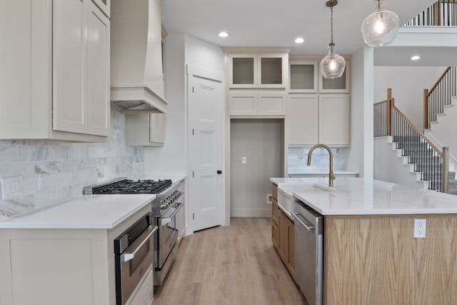 kitchen featuring pendant lighting, an island with sink, light hardwood / wood-style floors, custom range hood, and stainless steel appliances