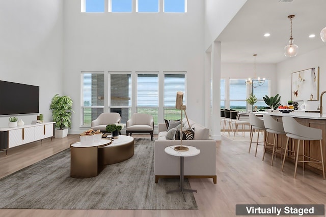 living room with a towering ceiling, a healthy amount of sunlight, a notable chandelier, and light hardwood / wood-style floors