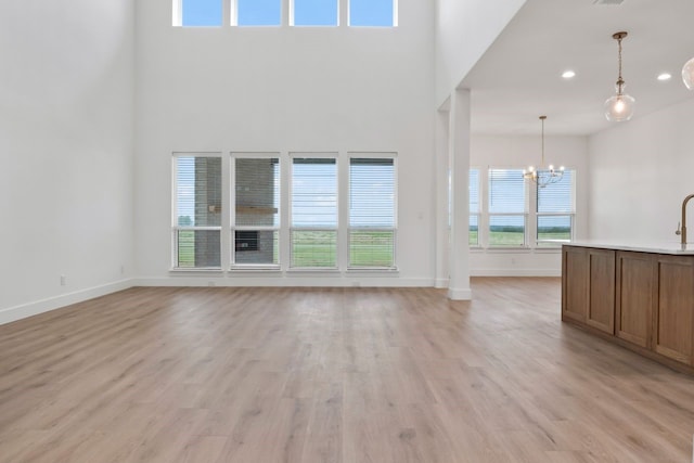 unfurnished living room featuring a notable chandelier, a healthy amount of sunlight, and light wood-type flooring