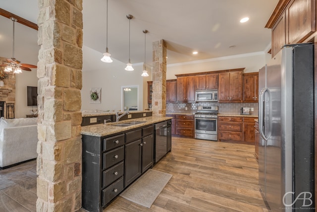 kitchen with appliances with stainless steel finishes, light wood-type flooring, backsplash, sink, and decorative light fixtures