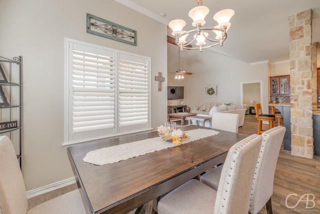 dining space featuring a stone fireplace, light hardwood / wood-style floors, ceiling fan with notable chandelier, and ornamental molding