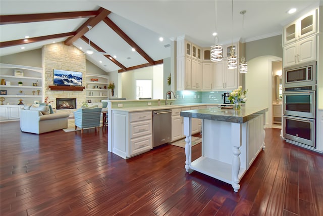 kitchen with a center island, a stone fireplace, appliances with stainless steel finishes, beamed ceiling, and dark hardwood / wood-style flooring