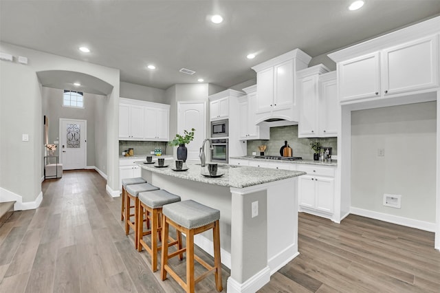 kitchen featuring appliances with stainless steel finishes, light hardwood / wood-style flooring, white cabinetry, and an island with sink