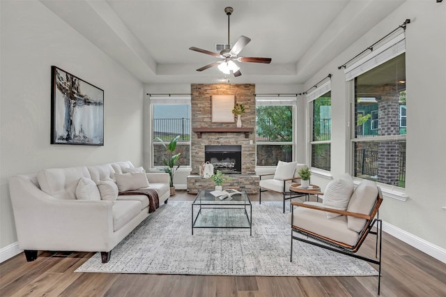 living room featuring hardwood / wood-style floors, ceiling fan, a stone fireplace, and a tray ceiling