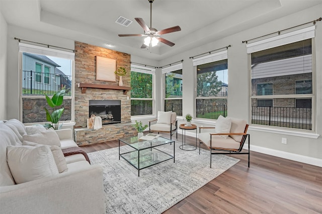 living room featuring ceiling fan, wood-type flooring, a fireplace, and a tray ceiling