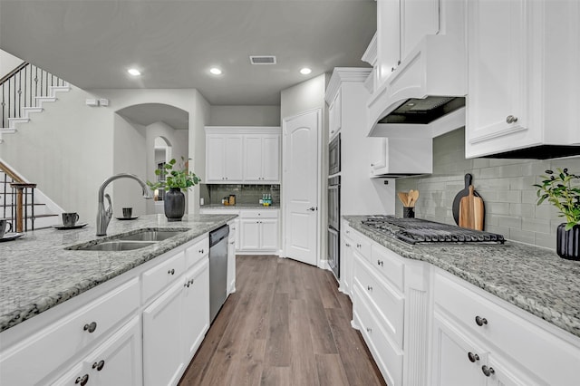 kitchen with appliances with stainless steel finishes, light stone counters, sink, wood-type flooring, and white cabinetry