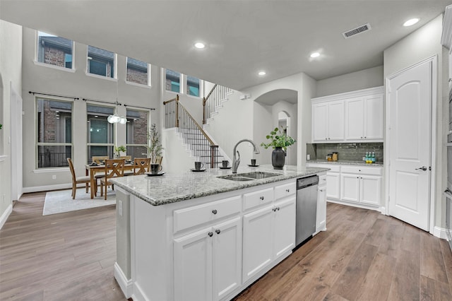 kitchen with white cabinetry, sink, stainless steel dishwasher, an island with sink, and light hardwood / wood-style floors