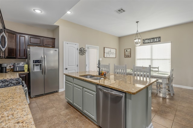 kitchen featuring sink, light stone countertops, an island with sink, appliances with stainless steel finishes, and dark brown cabinets