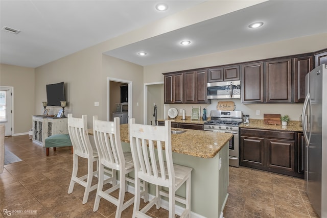 kitchen featuring a breakfast bar, sink, an island with sink, light stone counters, and stainless steel appliances