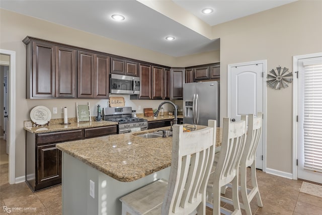 kitchen with a kitchen bar, dark brown cabinetry, stainless steel appliances, sink, and an island with sink