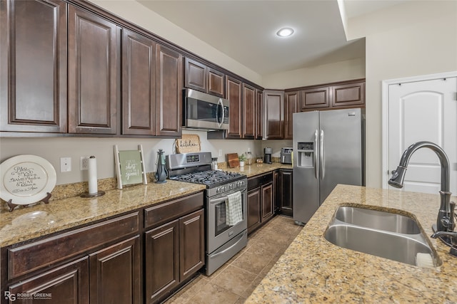 kitchen featuring dark brown cabinets, stainless steel appliances, light stone counters, and sink