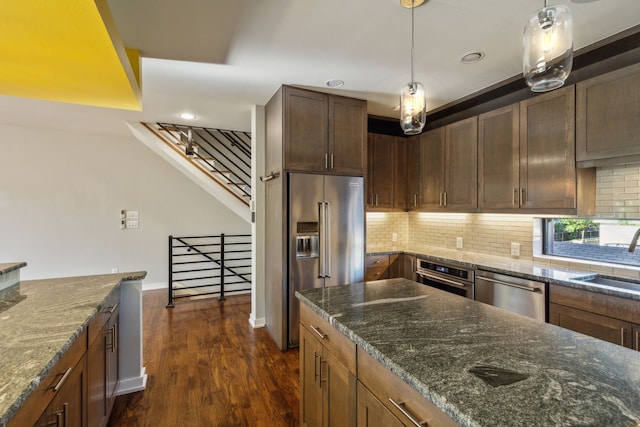 kitchen featuring hanging light fixtures, dark wood-type flooring, appliances with stainless steel finishes, and dark stone counters