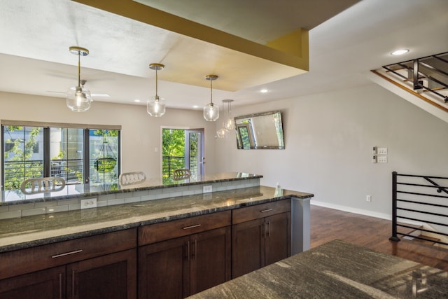 kitchen featuring dark stone counters, pendant lighting, dark wood-type flooring, and dark brown cabinets