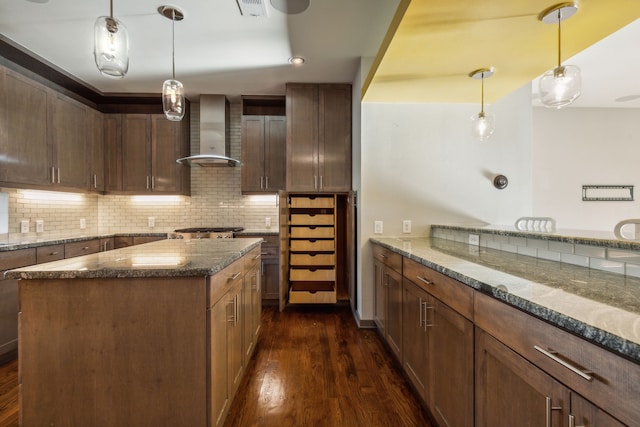 kitchen with dark stone countertops, dark hardwood / wood-style flooring, wall chimney exhaust hood, and a kitchen island