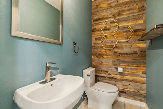 bathroom with sink, toilet, and wood walls