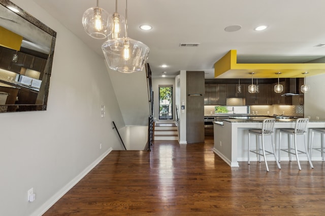 kitchen with dark brown cabinets, dark wood-type flooring, a breakfast bar area, and tasteful backsplash