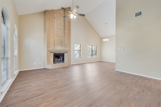 unfurnished living room featuring a brick fireplace, ceiling fan with notable chandelier, light hardwood / wood-style flooring, and high vaulted ceiling