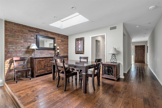 dining area featuring dark hardwood / wood-style flooring, a skylight, and brick wall