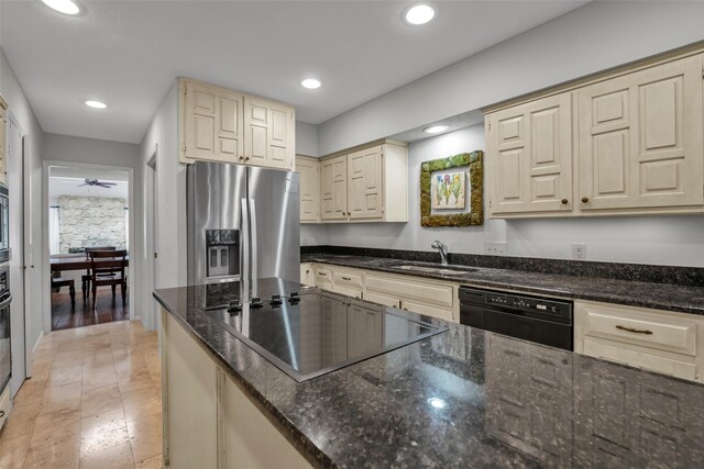 kitchen with black appliances, sink, ceiling fan, dark stone countertops, and cream cabinetry