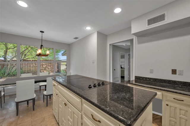 kitchen featuring black electric cooktop, cream cabinets, dark stone countertops, and a notable chandelier