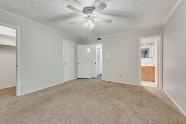 unfurnished bedroom featuring a textured ceiling, light colored carpet, ensuite bath, and ceiling fan