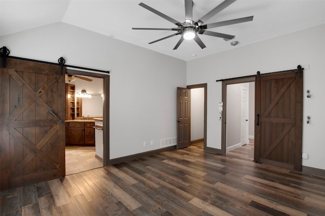 unfurnished bedroom featuring connected bathroom, ceiling fan, a barn door, dark hardwood / wood-style floors, and vaulted ceiling