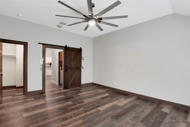 unfurnished bedroom with ceiling fan, a barn door, dark hardwood / wood-style floors, lofted ceiling, and a walk in closet