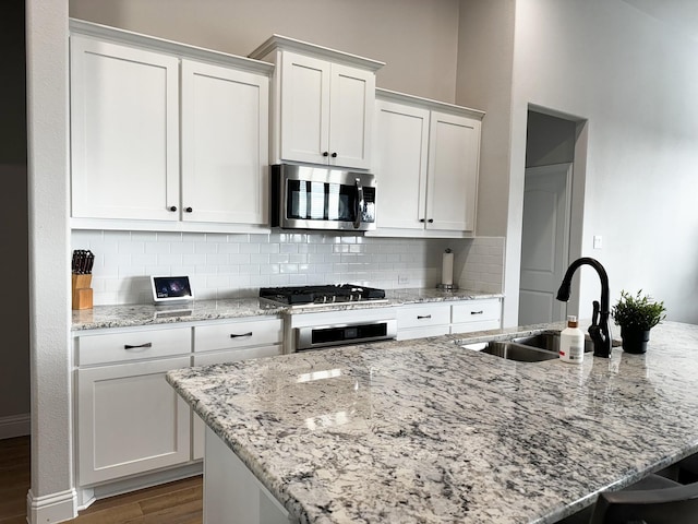 kitchen with appliances with stainless steel finishes, white cabinetry, sink, backsplash, and a kitchen island with sink