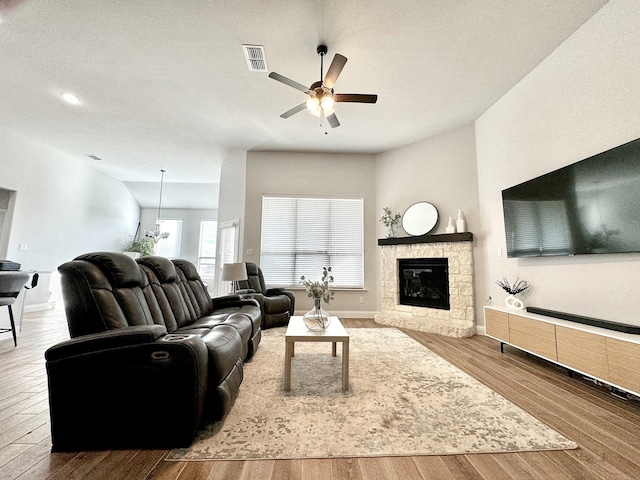 living room with ceiling fan, wood-type flooring, and a stone fireplace