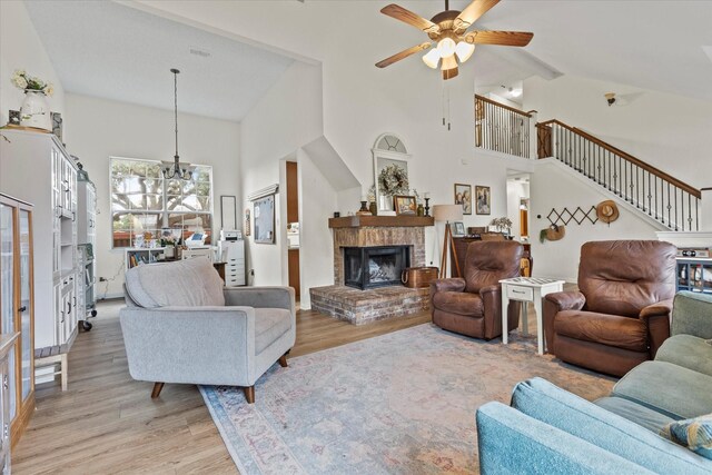 living room featuring a fireplace, high vaulted ceiling, ceiling fan with notable chandelier, and light wood-type flooring