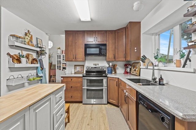 kitchen featuring black appliances, sink, light wood-type flooring, a textured ceiling, and butcher block countertops