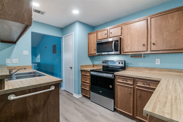 kitchen featuring sink, a textured ceiling, appliances with stainless steel finishes, light hardwood / wood-style floors, and butcher block counters