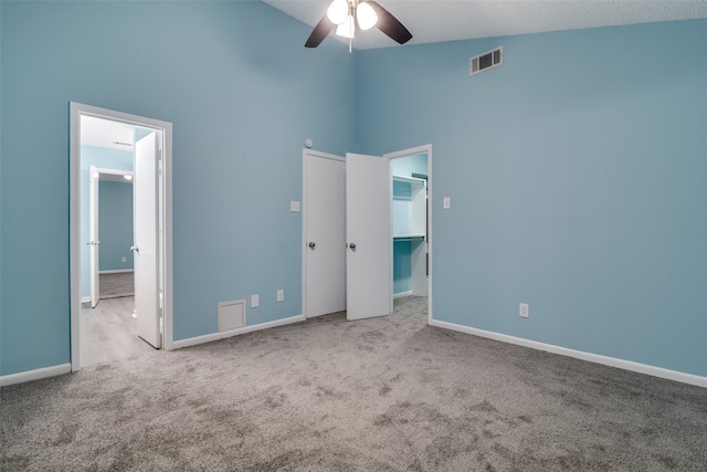 unfurnished bedroom featuring ceiling fan, light colored carpet, a walk in closet, and high vaulted ceiling