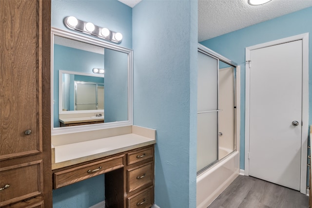 bathroom featuring vanity, combined bath / shower with glass door, wood-type flooring, and a textured ceiling