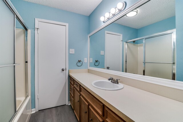 bathroom featuring vanity, combined bath / shower with glass door, wood-type flooring, and a textured ceiling