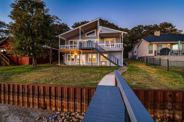 back house at dusk featuring a lawn and a deck