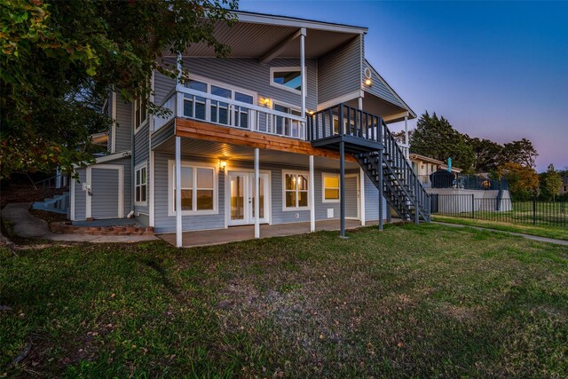 back house at dusk with french doors, a patio, a deck, and a lawn