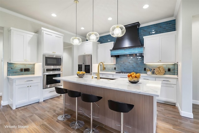 kitchen featuring premium range hood, sink, an island with sink, appliances with stainless steel finishes, and white cabinetry